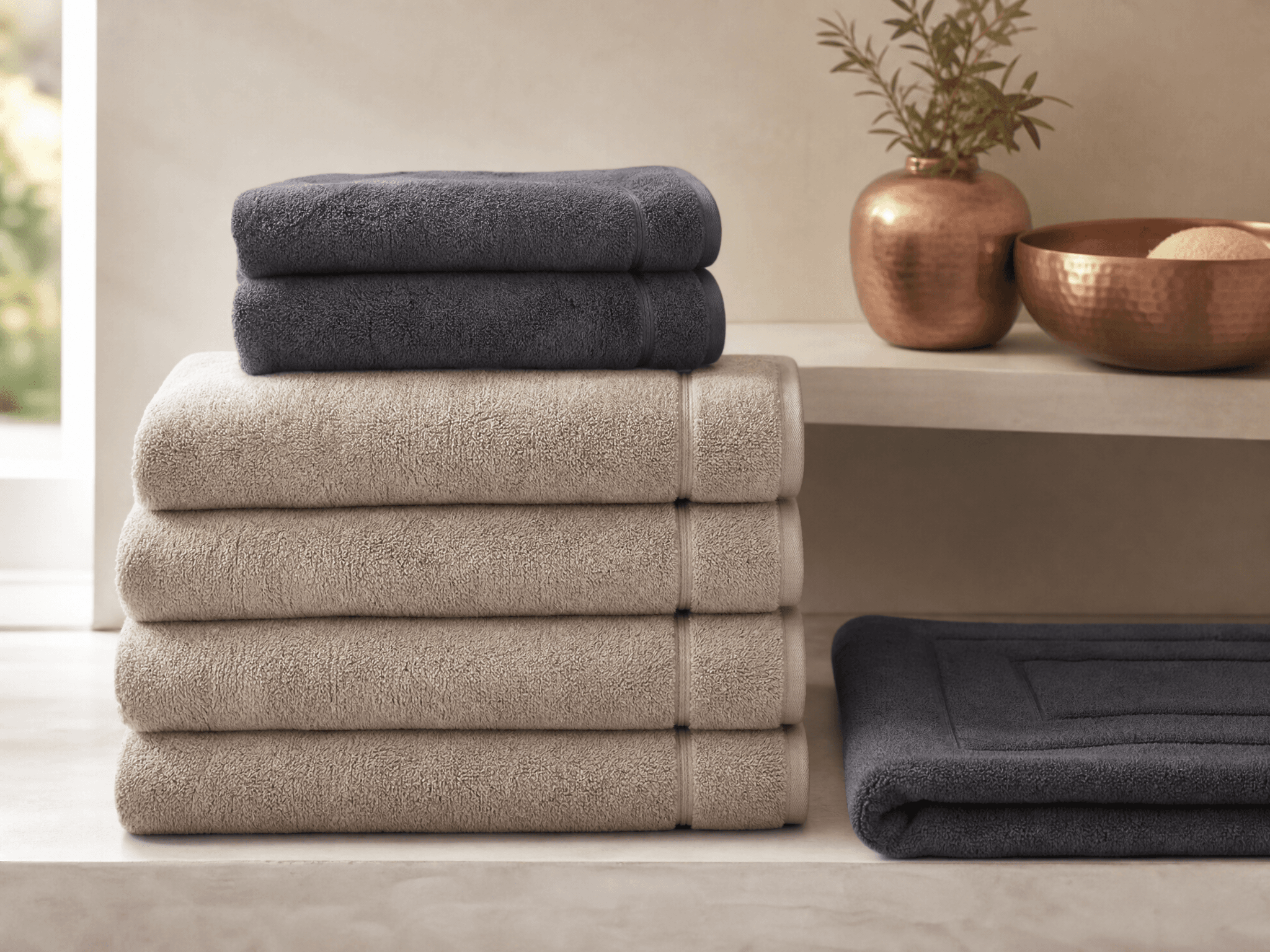 Stack of quick-dry bath towels and a folded bath mat on a bright bathroom shelf