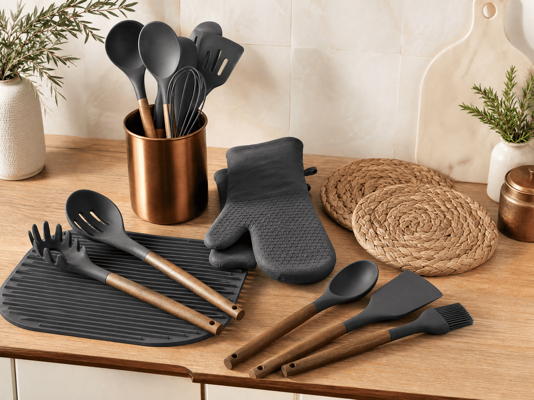 Matte silicone kitchen utensils with woven trivets and oven mitts on a kitchen counter